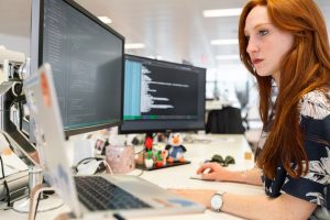 Mujer en una oficina, frente a pantallas de computadores trabajando con código de rpogramación